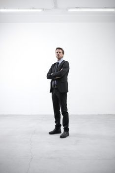 Confident businessman stannding in an empty open plan room with arms crossed.