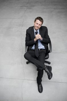 Businessman sitting on an office chair against concrete floor background.