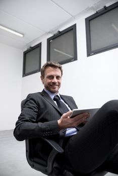 Smiling businessman at work holding a digital tablet with legs crossed.