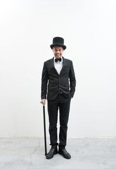 Classy smiling gentleman standing on white background and concrete floor in elegant suit with cane and bowler hat.