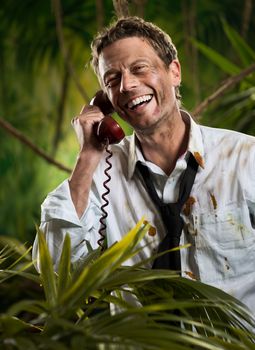 Attractive businessman talking on the phone in the jungle with torn clothing.