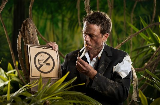 Businessman lost in jungle lighting a cigarette next to a no smoking sign.