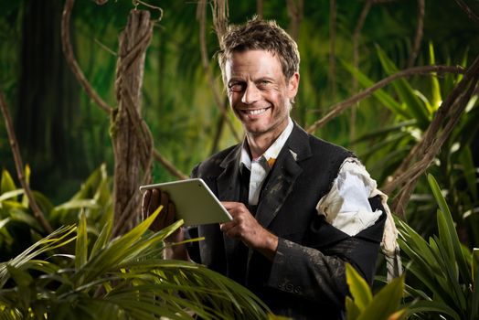 Businessman lost in jungle holding a digital tablet and smiling at camera
