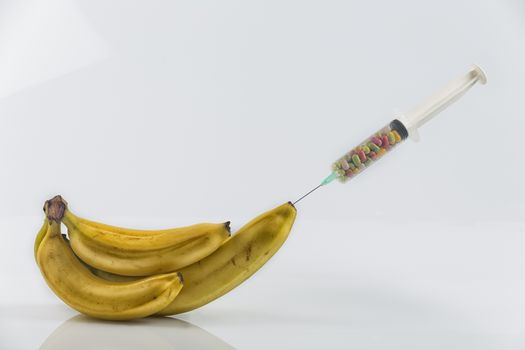 Male impotence metaphor: syringe with pills injecting into a  big banana among small bananas