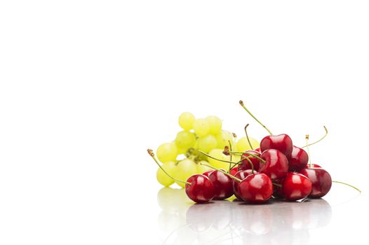 Heap of fresh organic ripe red cherries with a bunch green table grapes for a healthy vegetarian or vegan dessert on white with a reflection and plenty of copyspace
