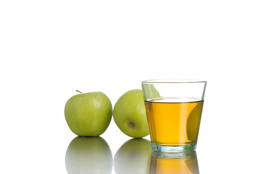 Small single glass with juice in front of two green apples on white background