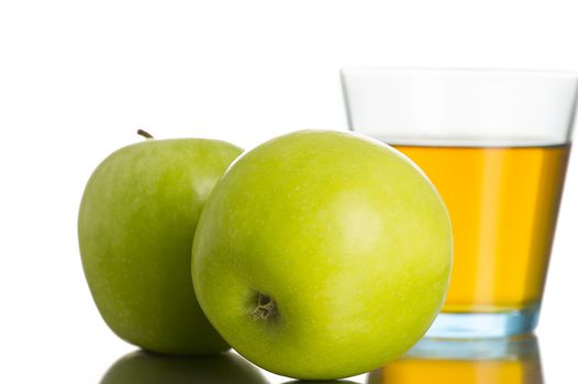 Close-up of two fresh Granny Smith green apples next to a glass of sweet tasty nutritious apple juice, with reflection, on white