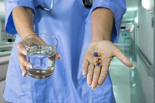 picture of doctor hands giving blue and orange pills and glass of water