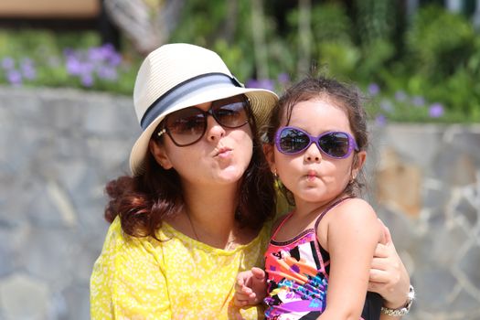 Portrait of mother and daughter giving a kiss to the camera. Focus in the little girl