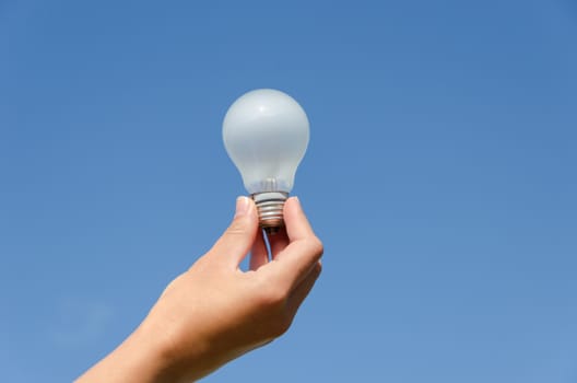 hand holding an incandescent light bulb on blue sky background