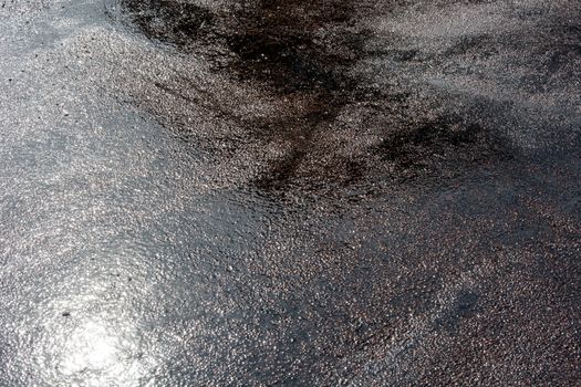 Wet asphalt background with reflections of the sun during a day after heavy rain