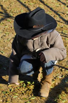 Young cowboy sitting and looking down at dirt