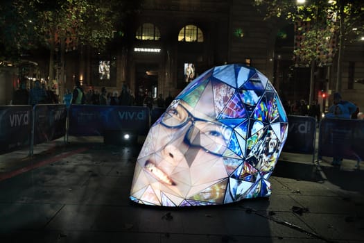 MARTIN PLACE, SYDNEY, AUSTRALIA - JUNE 6, 2014;  Locals and tourists ovserve and partiipate in  e|MERGEnce installation  in Martin Place, Sydney during Vivid Sydney annual festival event.  it is a huge, faceted head rising out of the pavement that comes to life withe personality by particupants using video capture technology.