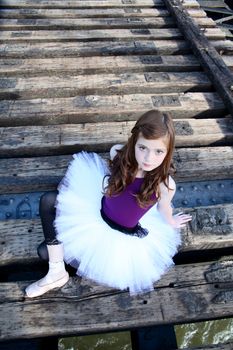 Beautiful girl wearing a white tutu sitting on a bridge