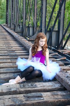 Beautiful girl wearing a white tutu sitting on a bridge