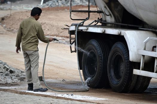 bandung, indonesia-june 9, 2014-man washing concrete mixer truck by spraying water into tire