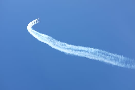 Vapour trails lead to a formation of red jet aircraft in display formation against a clear blue sky.