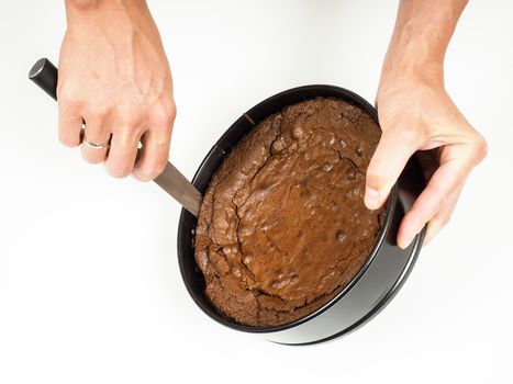 Person cutting out a freshly made chocolate cake from a round shaped rim