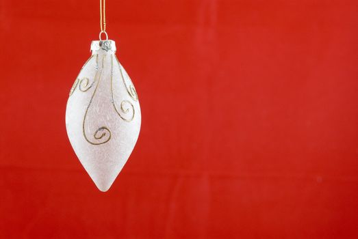 A white frosted glass Christmas decoration on red background