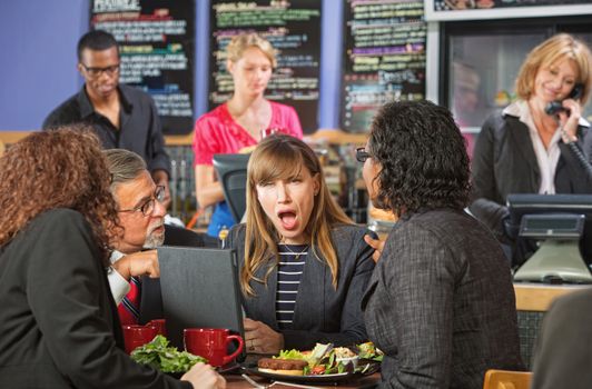 Shocked Hispanic woman in coffee house with coworkers