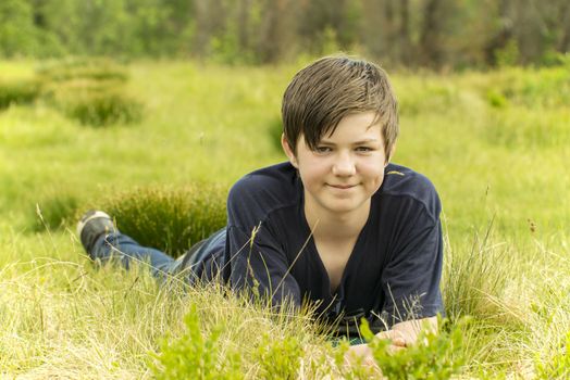 A happy teenager boy lying in grass