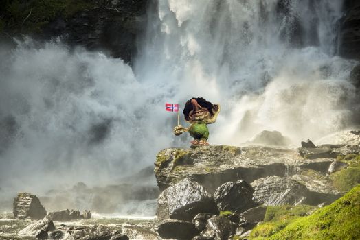 Huge waterfall against rocks. A troll  holding a Norwegian flag