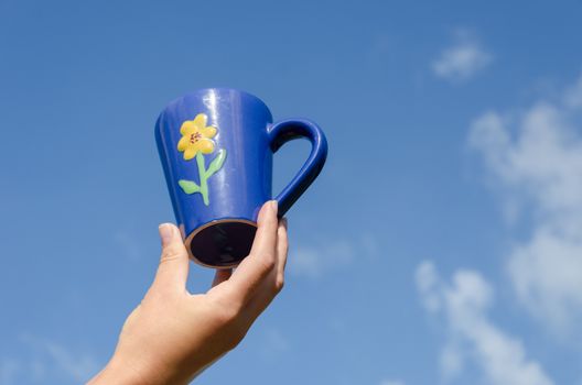 blue clay tea cup with flower in hand on blue sky background