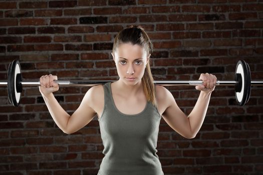 Portrait of Sweat fit woman lifting dumbbells on brick background 