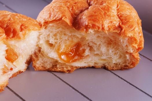 Open croissant with apricot jam, over wooden table