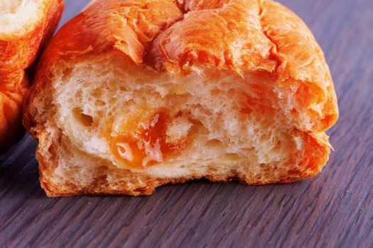 Open croissant with apricot jam, over wooden table