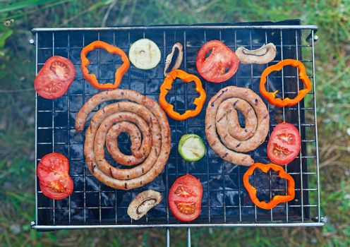 Barbecue on a hot day during the summer vacation on a green grass background. Meat and vegetables on the grill.