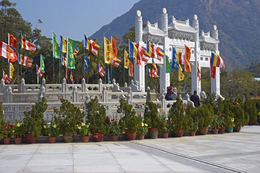 Ornate white stone gateway adorned with colorful flags at the Po Lin Buddhist monastery located on Ngong Ping Plateau on Lantau Island, Hong Kong, China