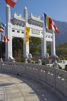 Ornate white stone gateway adorned with colorful flags at the Po Lin Buddhist monastery located on Ngong Ping Plateau on Lantau Island, Hong Kong, China
