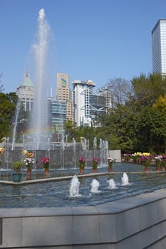 Colorful flowers and fountains in the Botanical Gardens surrounded by tall office buildings in Hong Kong, China.