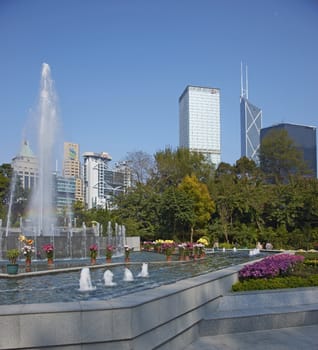 Colorful flowers and fountains in the Botanical Gardens surrounded by tall office buildings in Hong Kong, China.