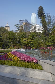Colorful flowers and fountains in the Botanical Gardens surrounded by tall office buildings in Hong Kong, China.