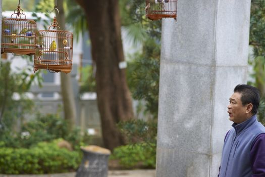 Man whistling to a caged song bird in the Yuen Po Street Bird Garden in Kowloon, Hong Kong.
