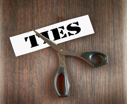 Scissors cutting the word "Ties" written on a paper strip, over wooden background