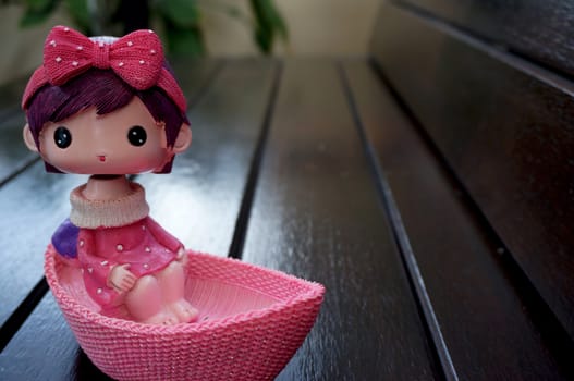 Ceramic doll is a girl wearing a pink dress and headband in the boat. Placed on a wooden chair on the morning, in the backyard.                              