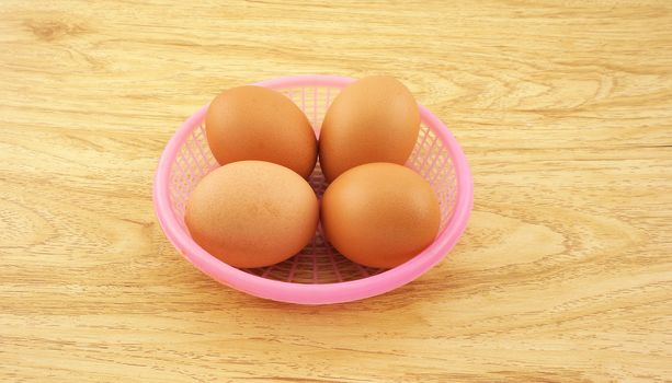 Four fresh eggs in a pink small basket, placed on a brown wooden table .                               