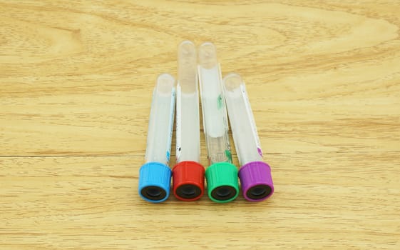 Blood sampling tube put on the wooden table, cap test tubes with four colors: blue, red, green, and purple.                        