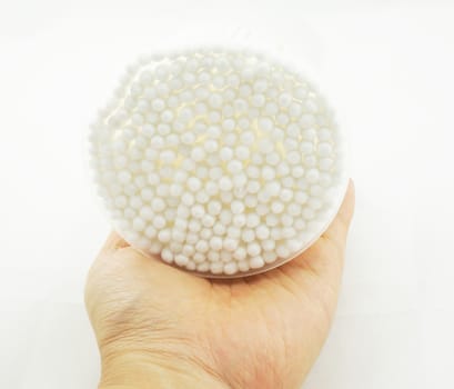 Hand is holding white cotton bud,  packed in clear plastic  round box.                              