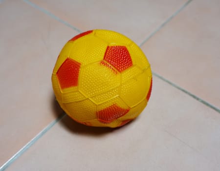 Soccer ball in yellow color with small red stripes. Placed on the floor at home                               
