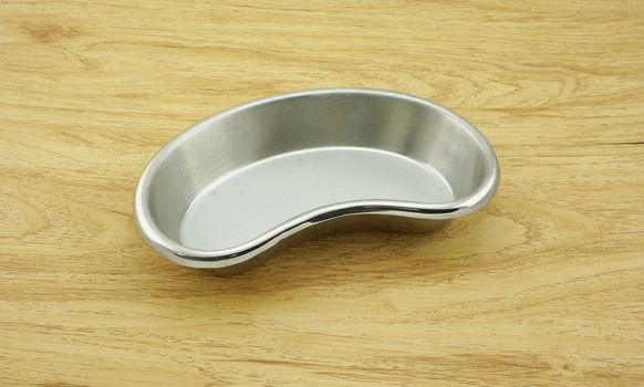 Kidney-shaped bowl, a stainless steel container, placed on a  light brown wooden table.