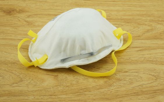 The N95 mask, bulbous white circle shape. Earhook sides have a yellow belt, placed on a wooden table.                                  