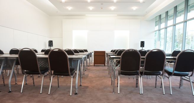  Classrooms on campus have a white background instead of a chalkboard, a desk, a chair and a table in the middle for placing overhead. The exterior is glass overlooking the outside.                              