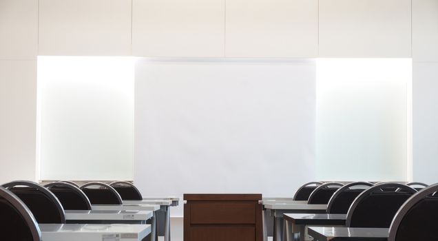 Classrooms on campus have a white background instead of a chalkboard, a desk, a chair and a table in the middle for placing overhead.                              