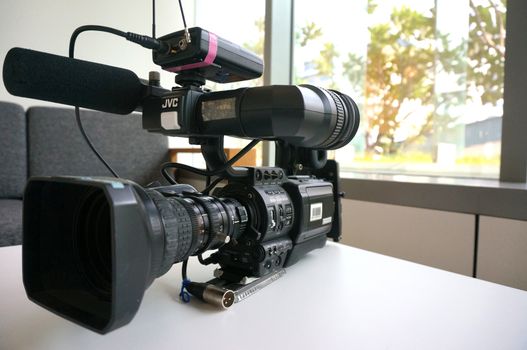 Big black video camera, placed on a white table at office.                            