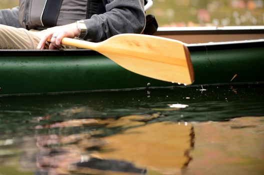 close-up image of a man on a river in a green canoe with a wooden paddle