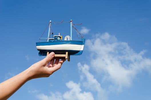 female hand hold small wooden ship toy model on blue sky background